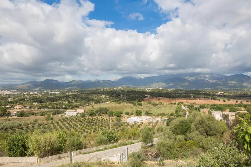 Un paisaje rural con campos cultivados, edificios dispersos y montañas lejanas bajo un cielo nublado.