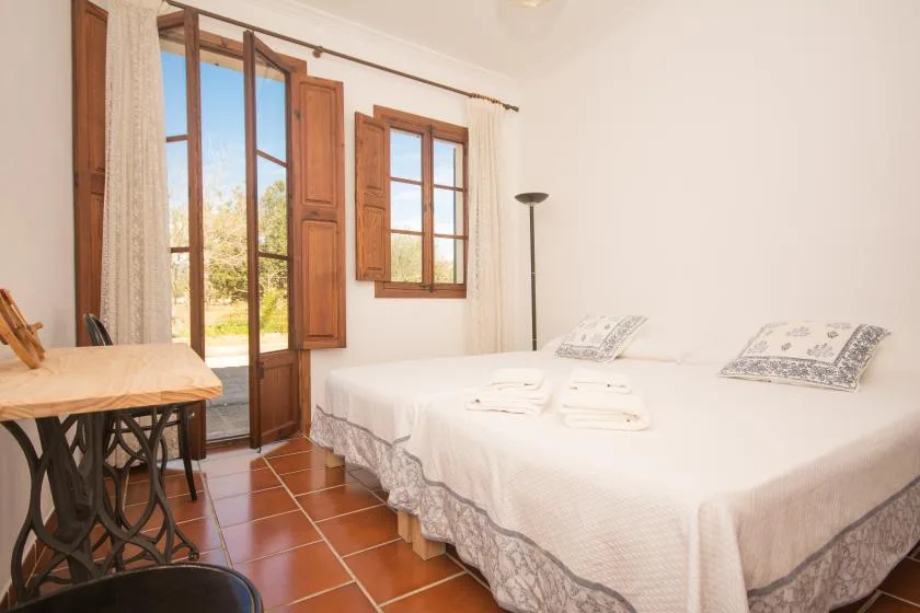Un dormitorio luminoso con ropa de cama blanca, contraventanas de madera y una puerta acristalada al exterior.