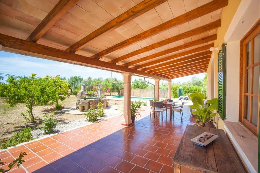 Un patio cubierto con suelo de baldosas, mesa de comedor exterior y vistas al jardín.