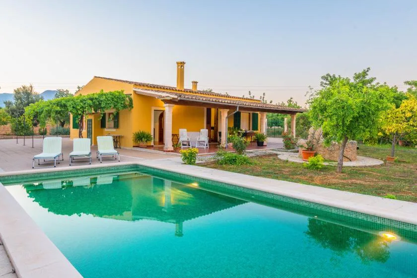 A swimming pool beside a yellow house and leafy garden.