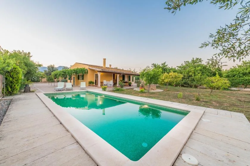 Outdoor swimming pool beside a low house, with greenery surrounding the patio.