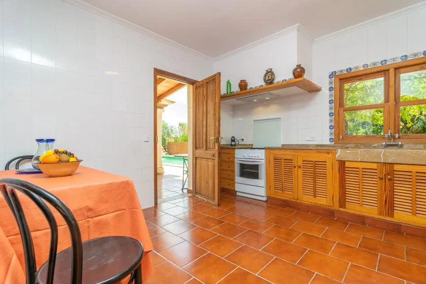 Una cocina con azulejos, armarios de madera, una ventana y una mesa cubierta con un mantel naranja.