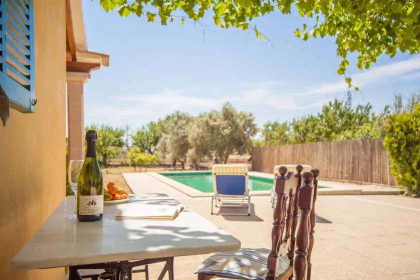 Un patio soleado junto a la piscina, con una mesa al lado del agua.