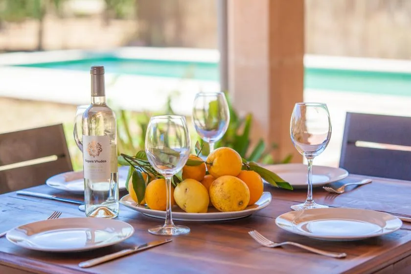 Una mesa puesta tiene cítricos y copas de vino junto a una piscina.