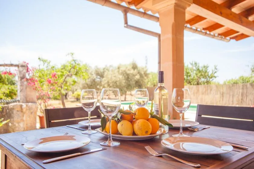 Una mesa de comedor en el patio está preparada con platos, copas y un cuenco de cítricos.