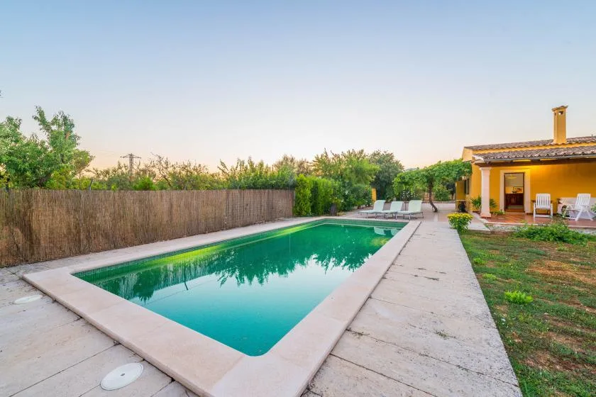Una piscina junto a un patio pavimentado y un edificio pequeño.