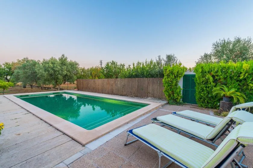 Una piscina al aire libre está junto a un patio pavimentado con tumbonas reclinables.