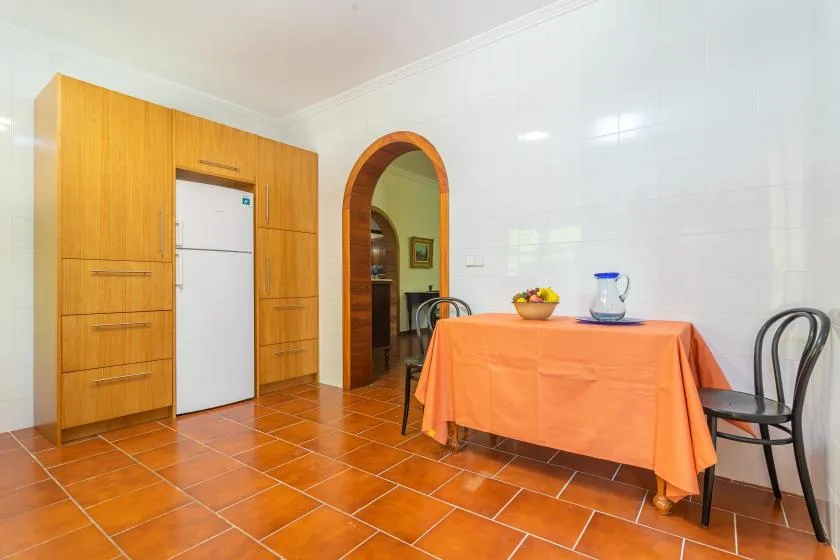 Un comedor con suelo de baldosas, mesa, sillas y refrigerador empotrado.