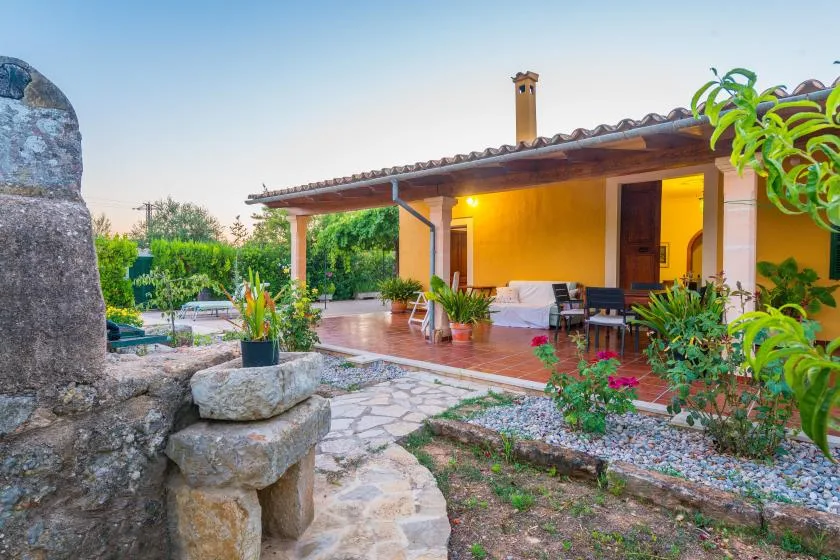 Un patio cubierto con asientos al aire libre y plantas en macetas junto a un jardín.