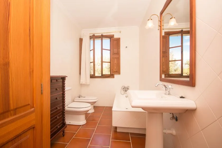 Un baño con lavabo, inodoro y ventanas con marcos de madera.