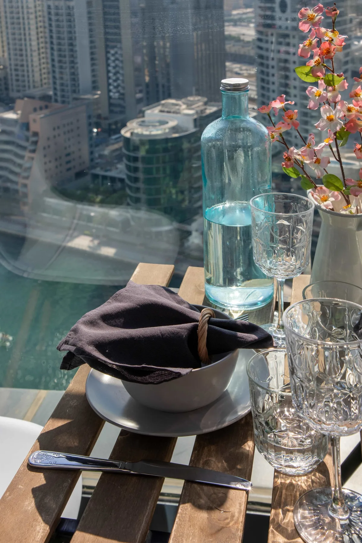 Una mesa de comedor junto a una ventana tiene vasos y un cuenco con una servilleta doblada.