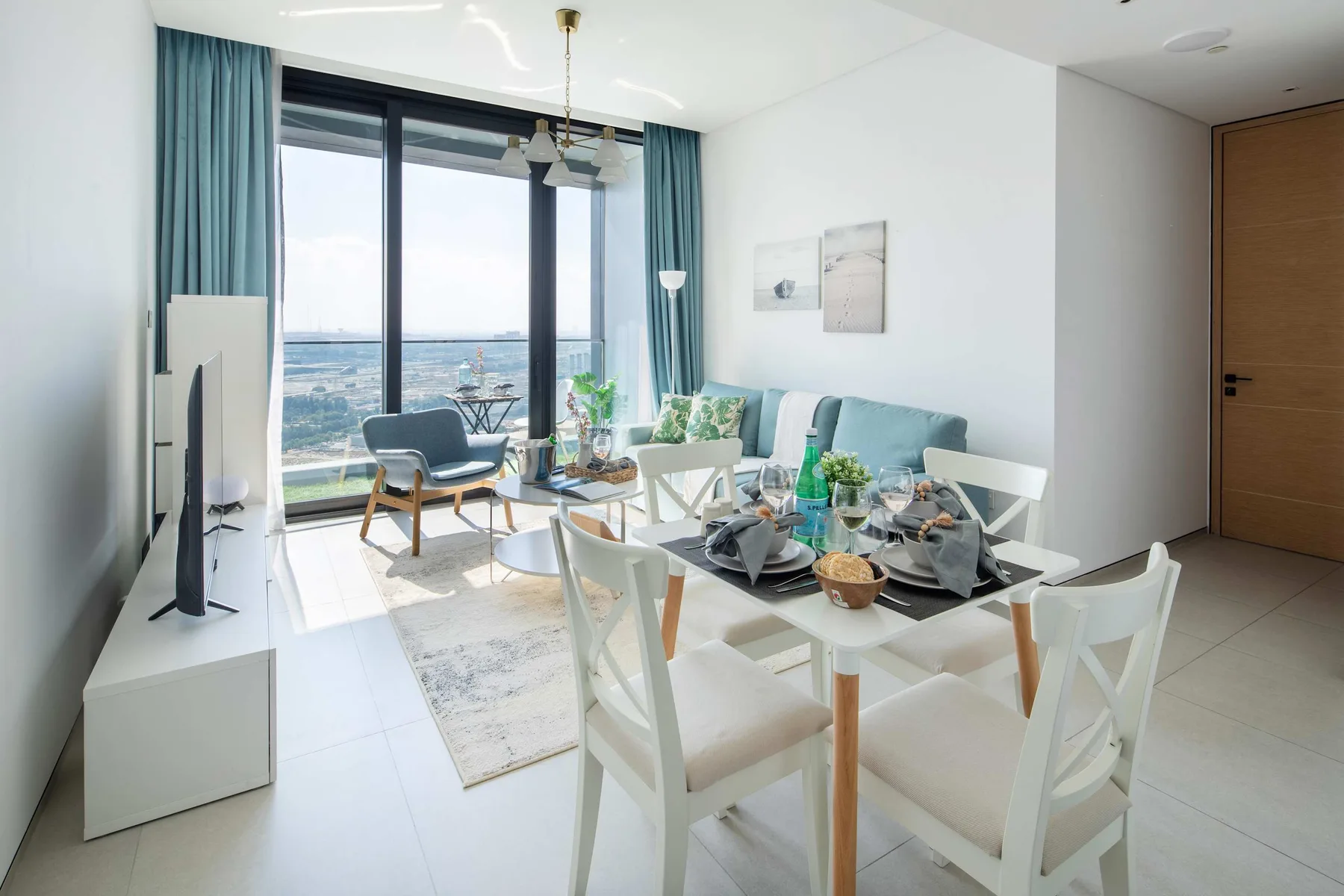 Un comedor luminoso con la mesa puesta junto a grandes ventanales y cortinas color turquesa.