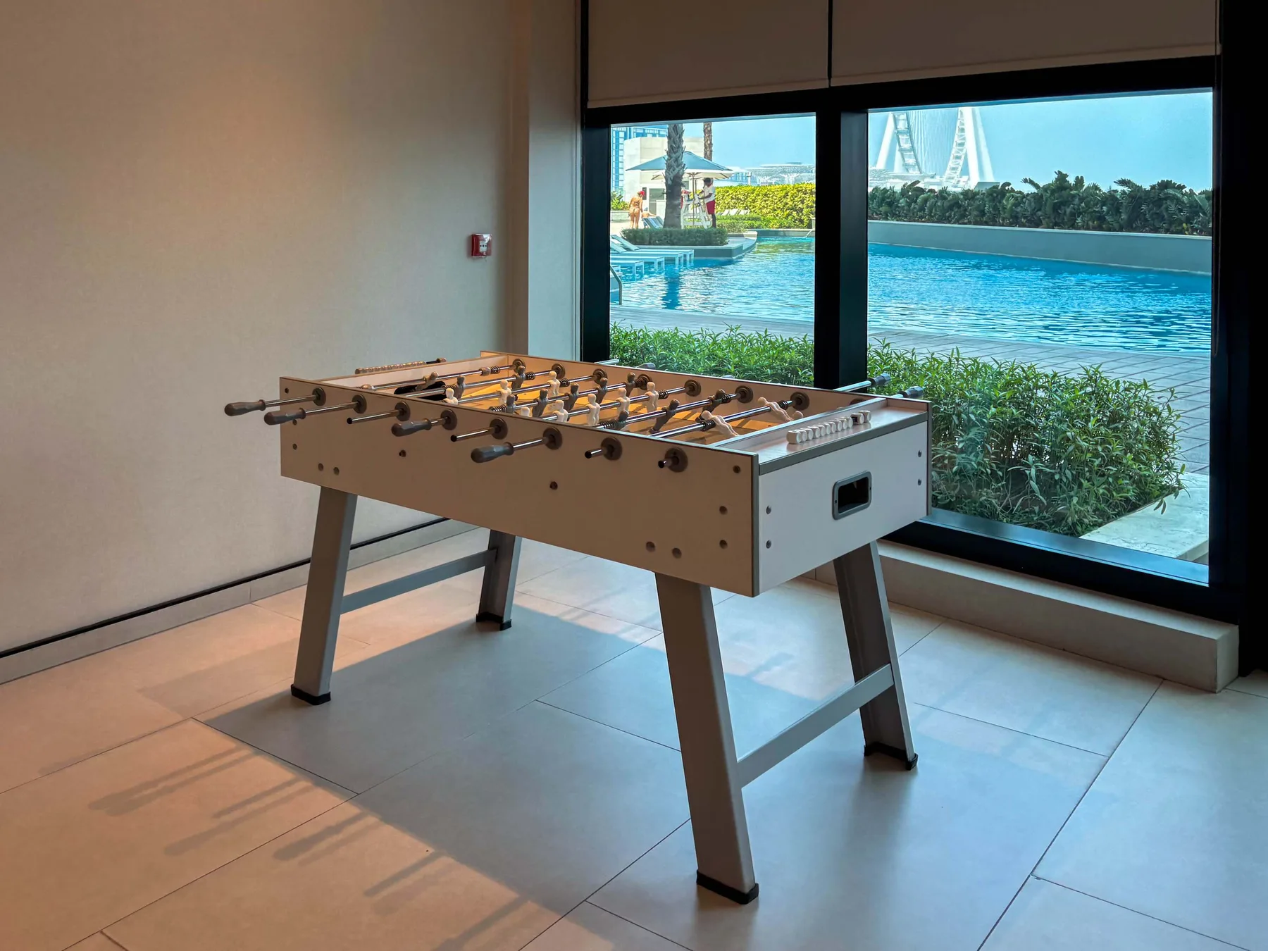 Un futbolín está junto a grandes ventanas con vistas a una piscina y al agua.