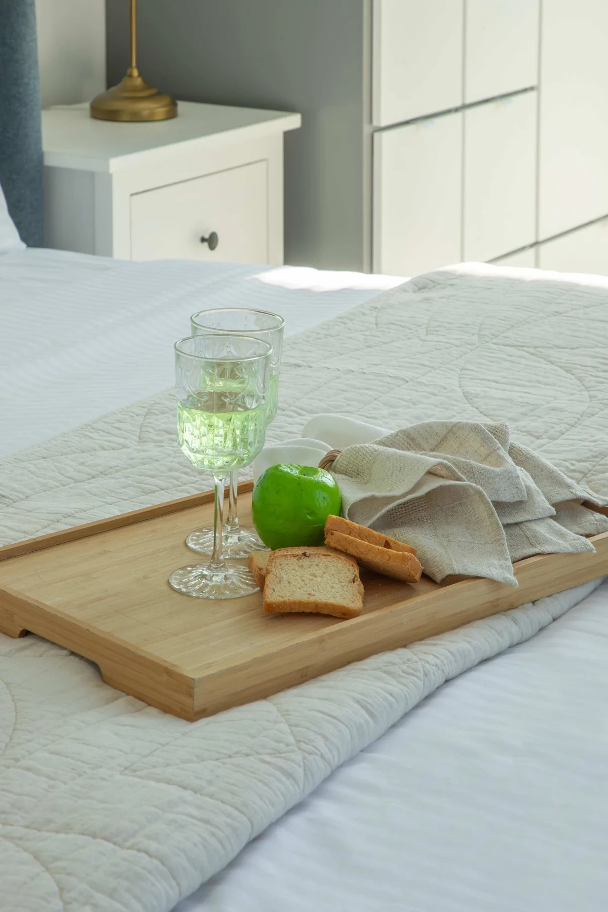 Una cama bien tendida con una bandeja de madera que sostiene una bebida, una lima y pan.