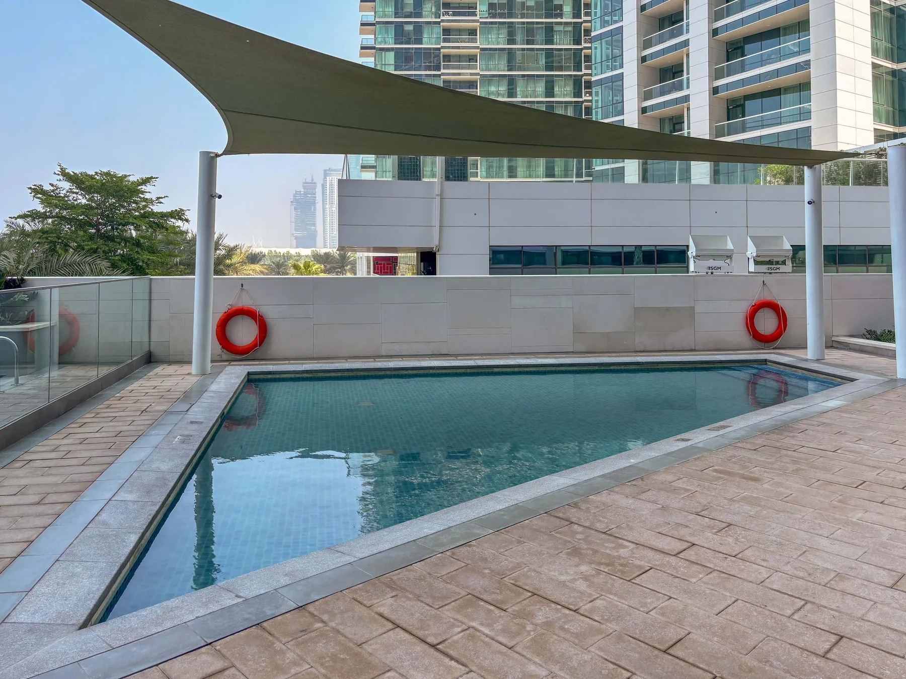 Una piscina al aire libre está bajo una cubierta de sombra junto a edificios altos.