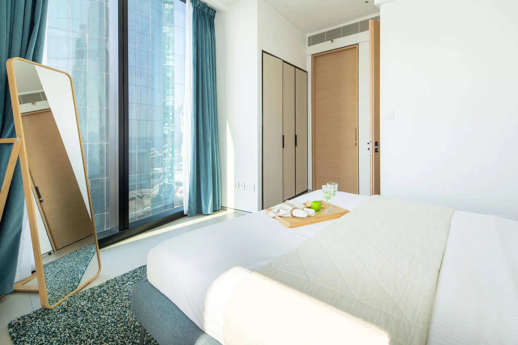Un dormitorio luminoso con una cama junto a ventanas altas y cortinas azules.