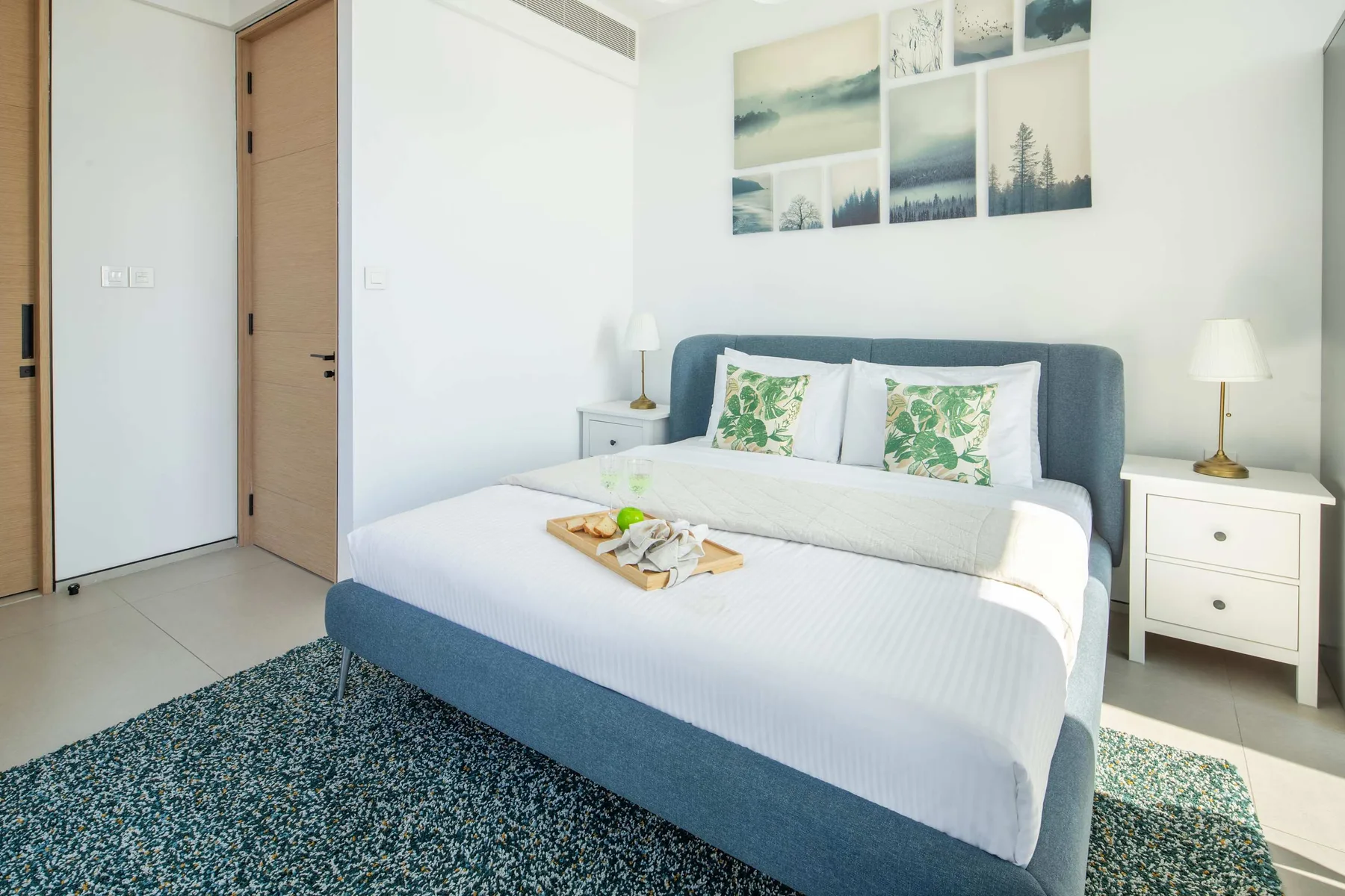 Un dormitorio luminoso con una cama grande, almohadas estampadas con hojas y paisajes sobre el cabecero.