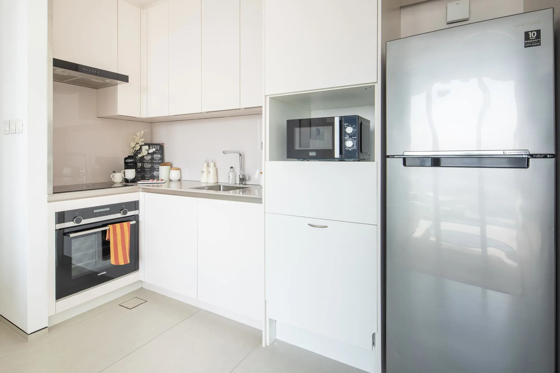 Una cocina luminosa con gabinetes blancos, horno, microondas y refrigerador.