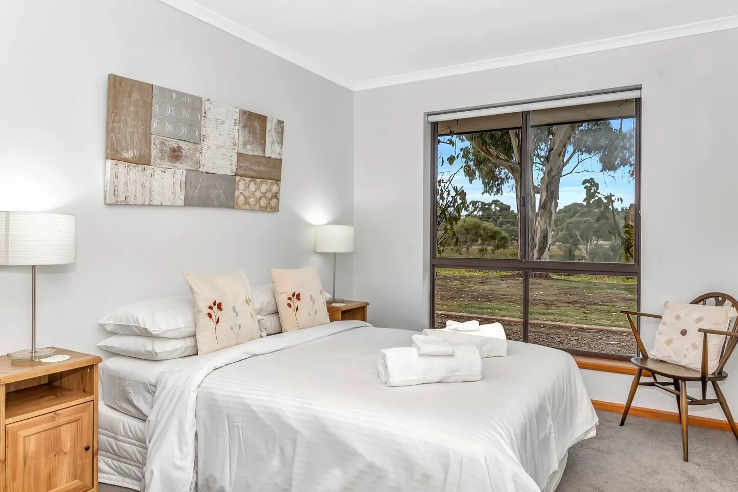 A bright bedroom with a neatly made bed and a large window overlooking trees.