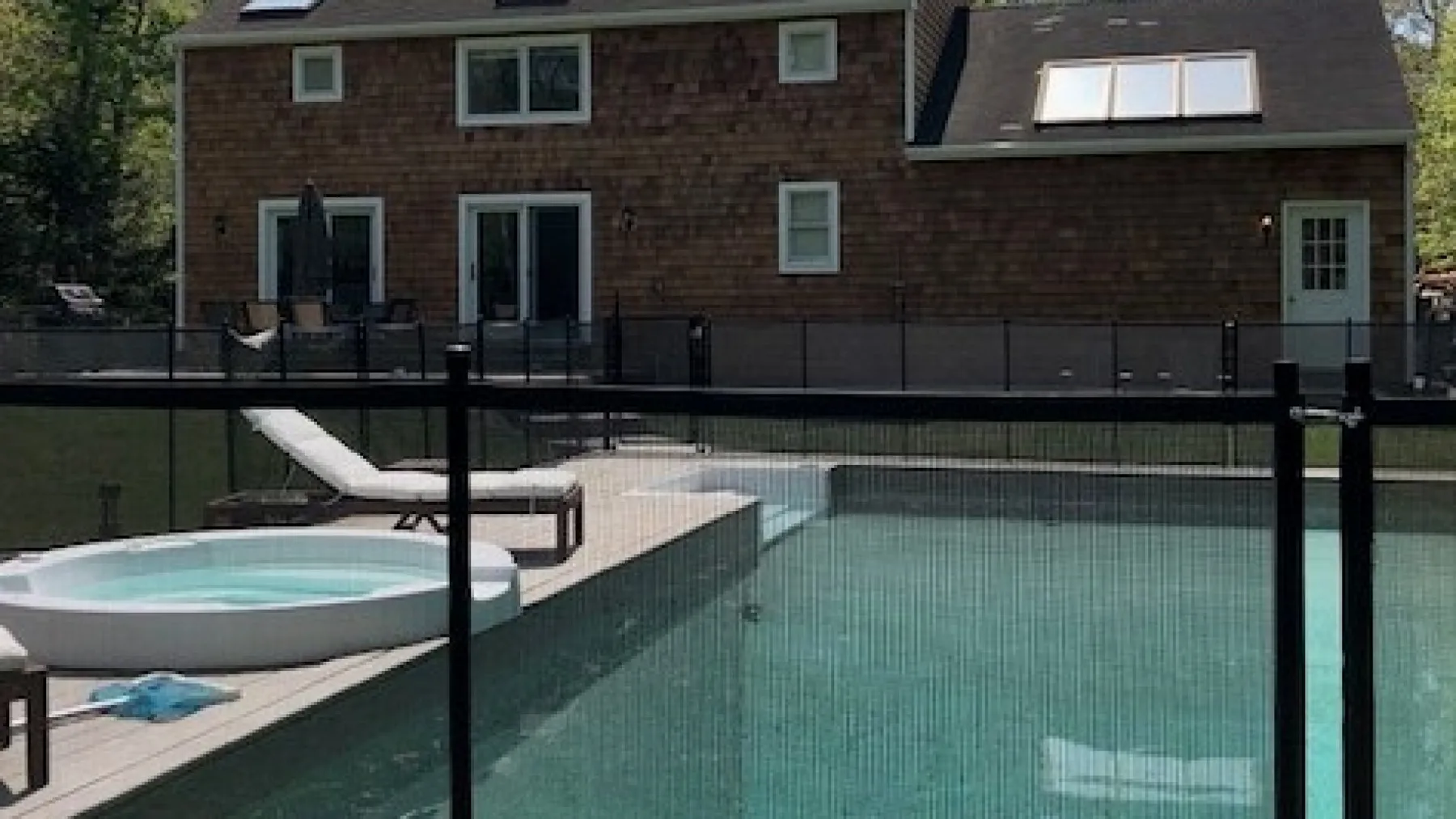 A backyard pool and hot tub sit beside a brick house.
