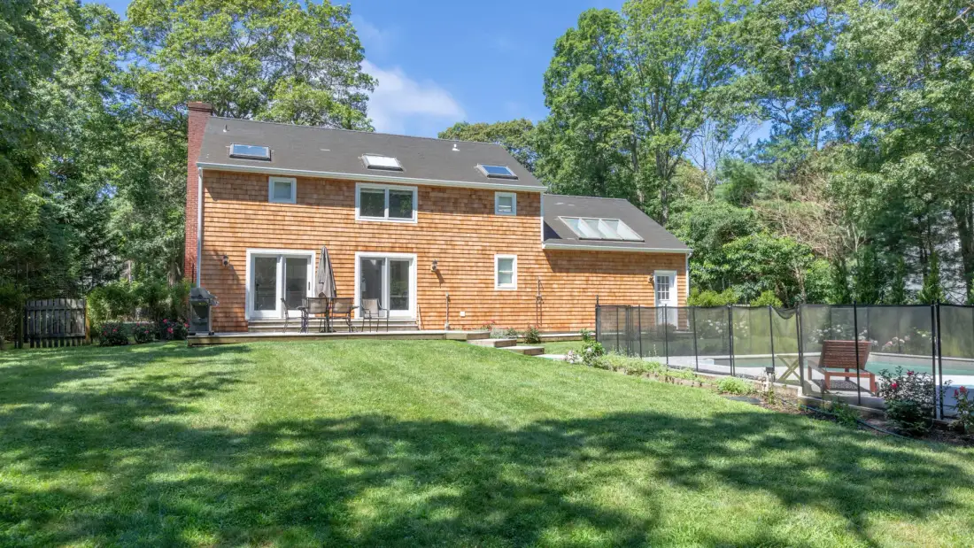 A two-story house stands beside a fenced outdoor area and green lawn.
