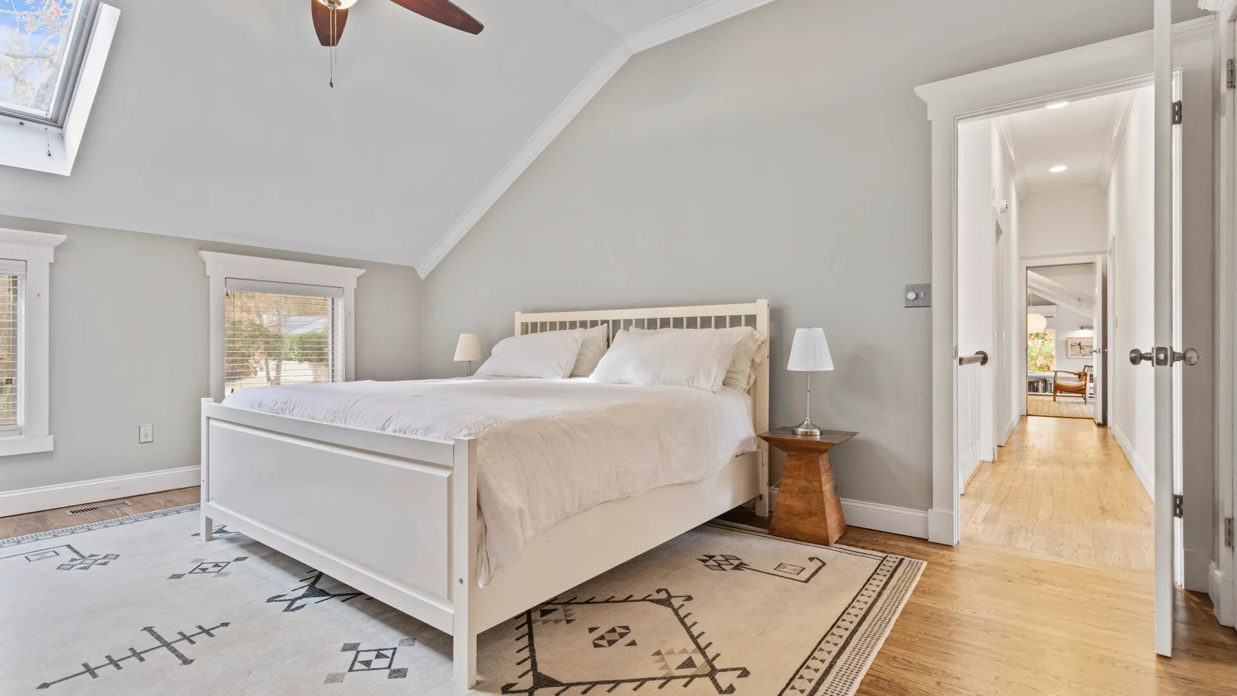 A bright bedroom with a large bed, patterned rug, and open doorway.