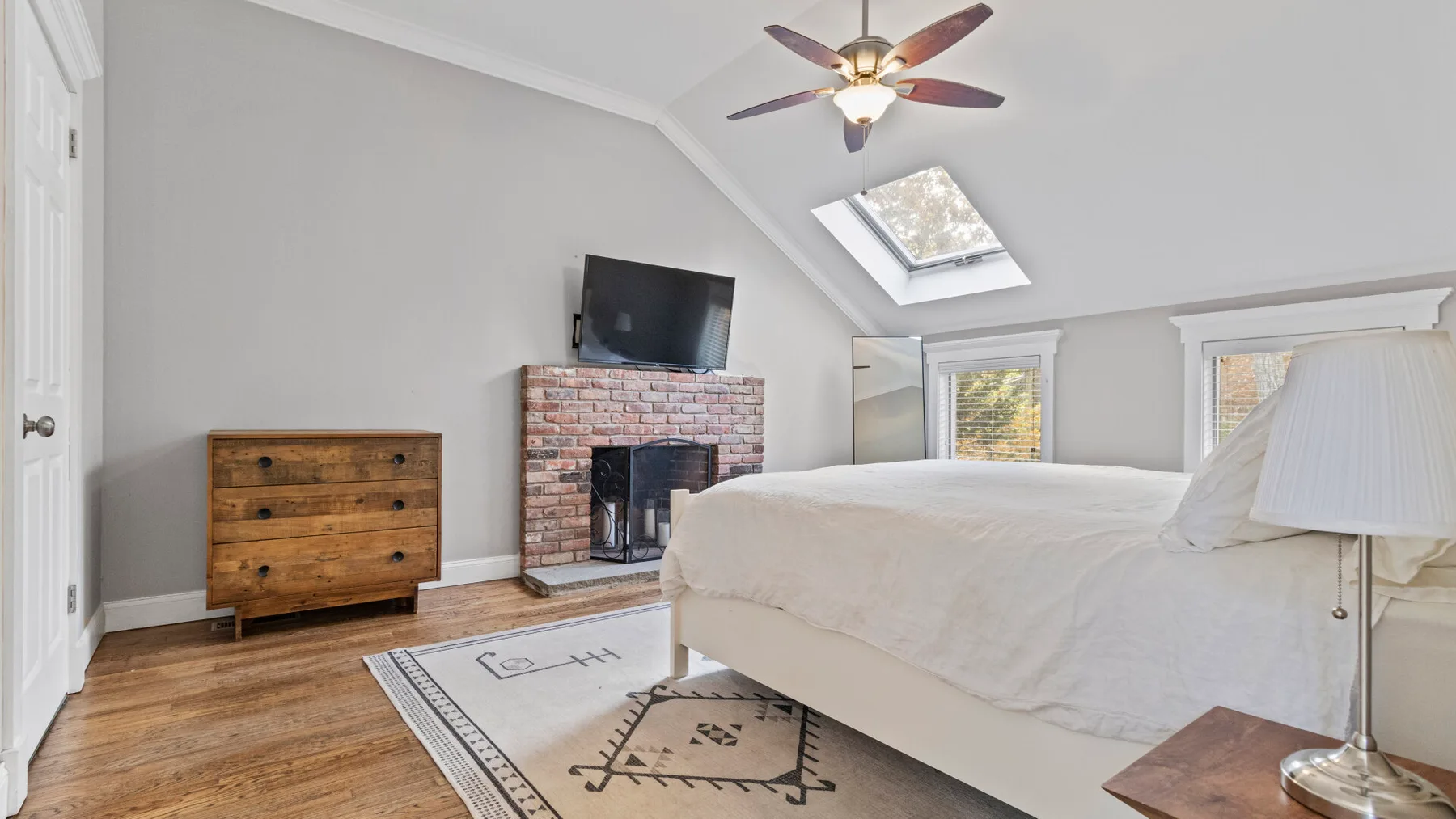 A bedroom with a bed, brick fireplace, and sloped ceiling.