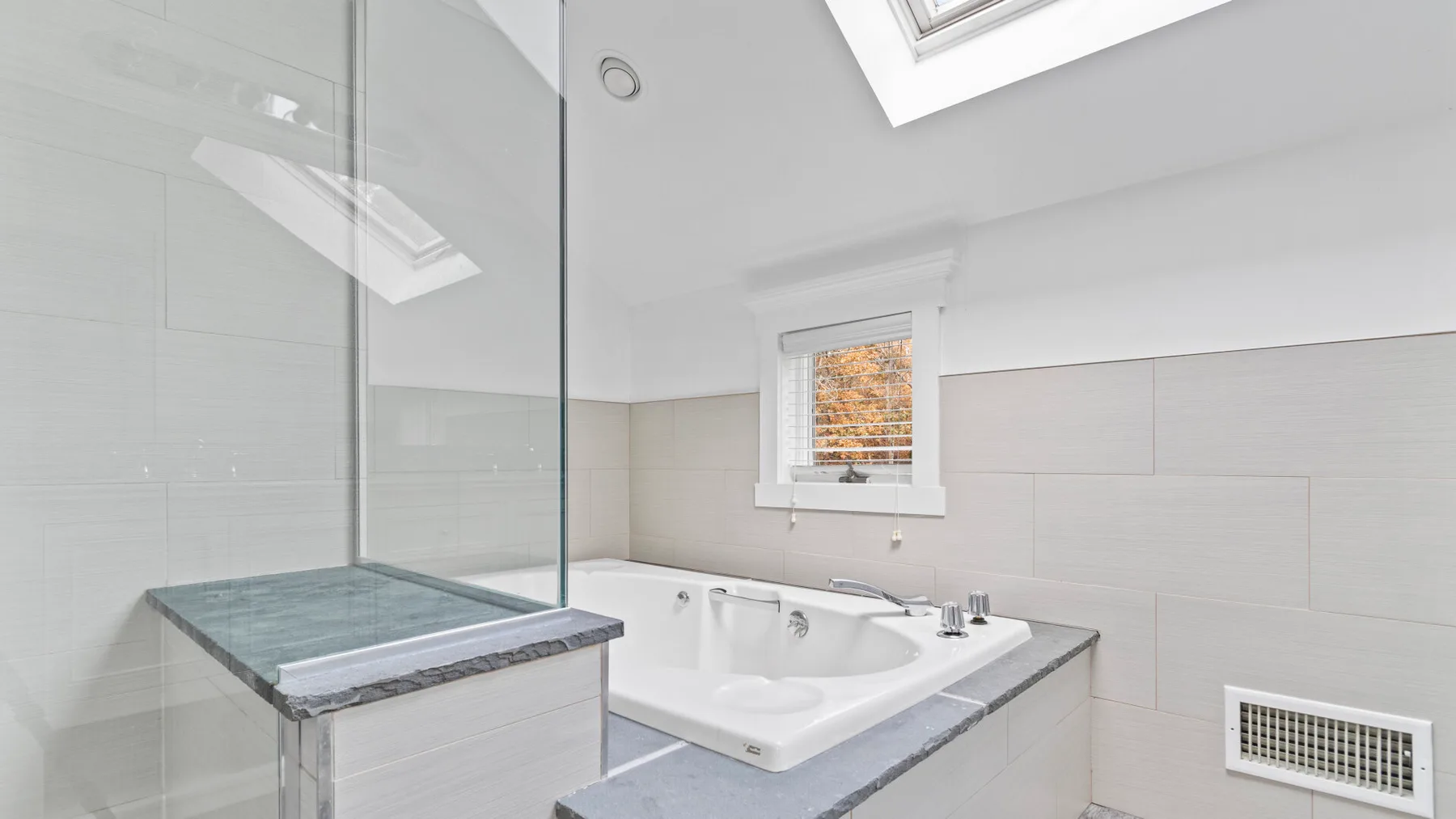 A bright bathroom with a bathtub, glass shower screen, and skylight.