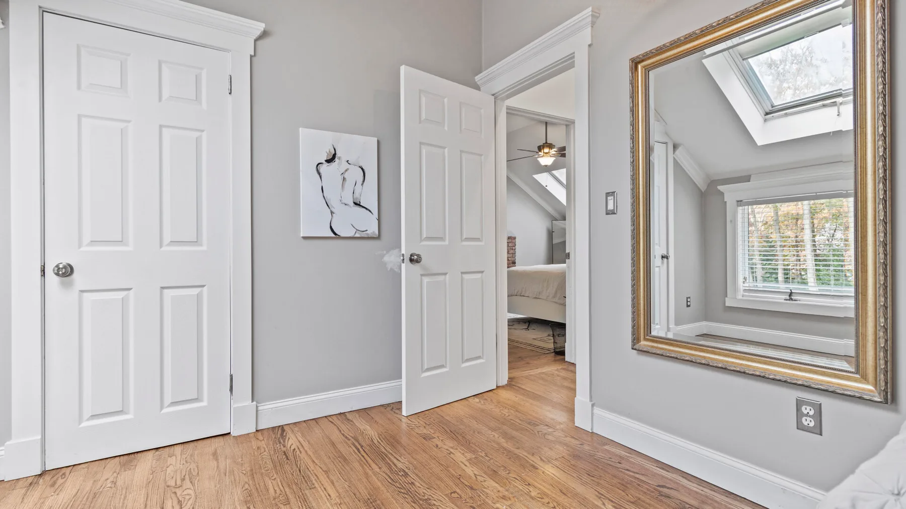A bright interior hallway with white doors and a framed mirror.