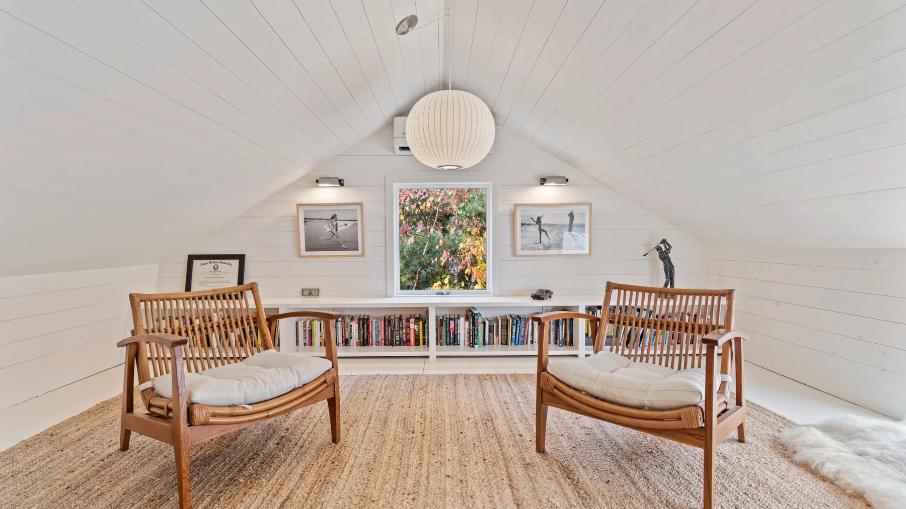 An attic sitting area with two wooden seats and a low bookshelf.