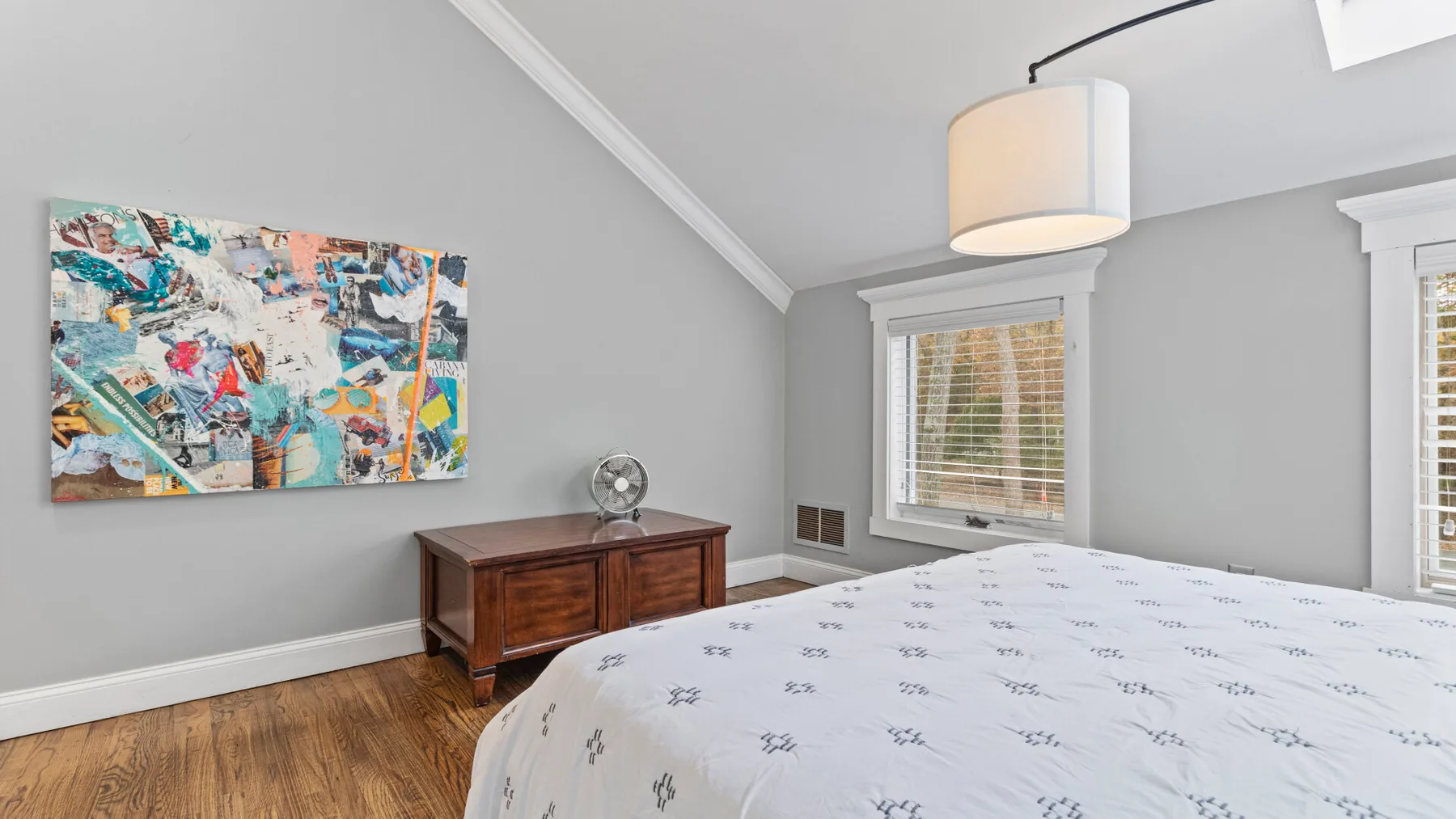 A bedroom with a bed, wooden dresser, and colorful artwork on the wall.