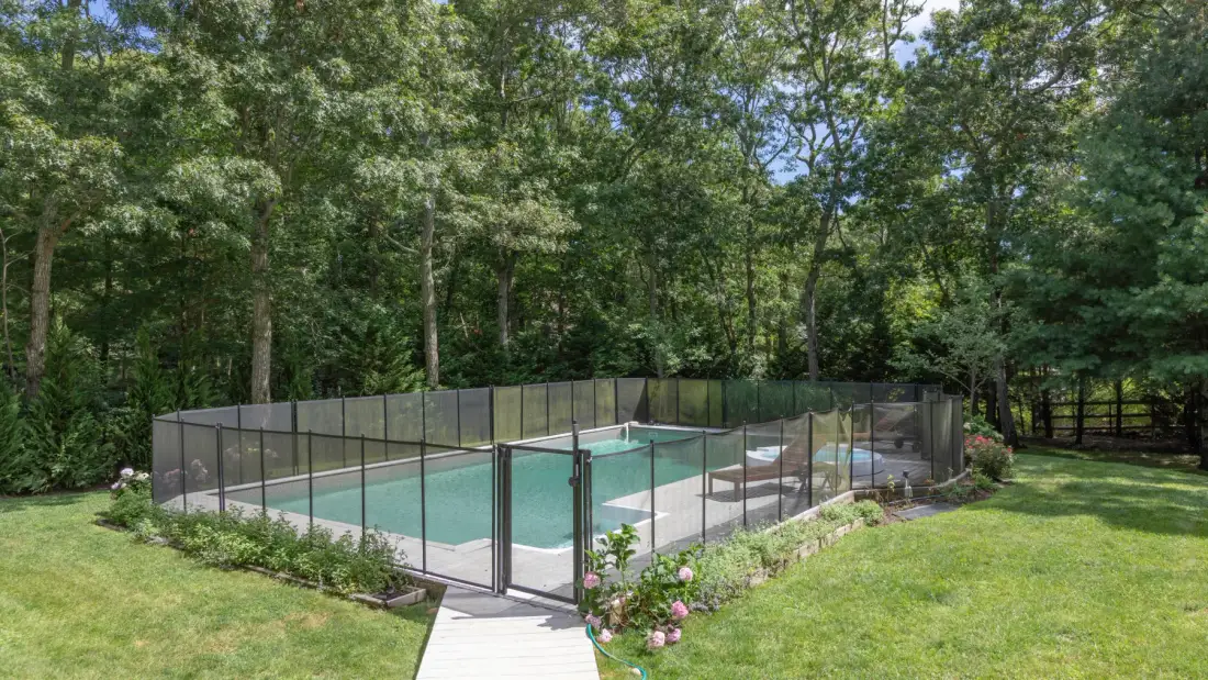 An outdoor swimming pool is enclosed by a glass fence and surrounded by trees.