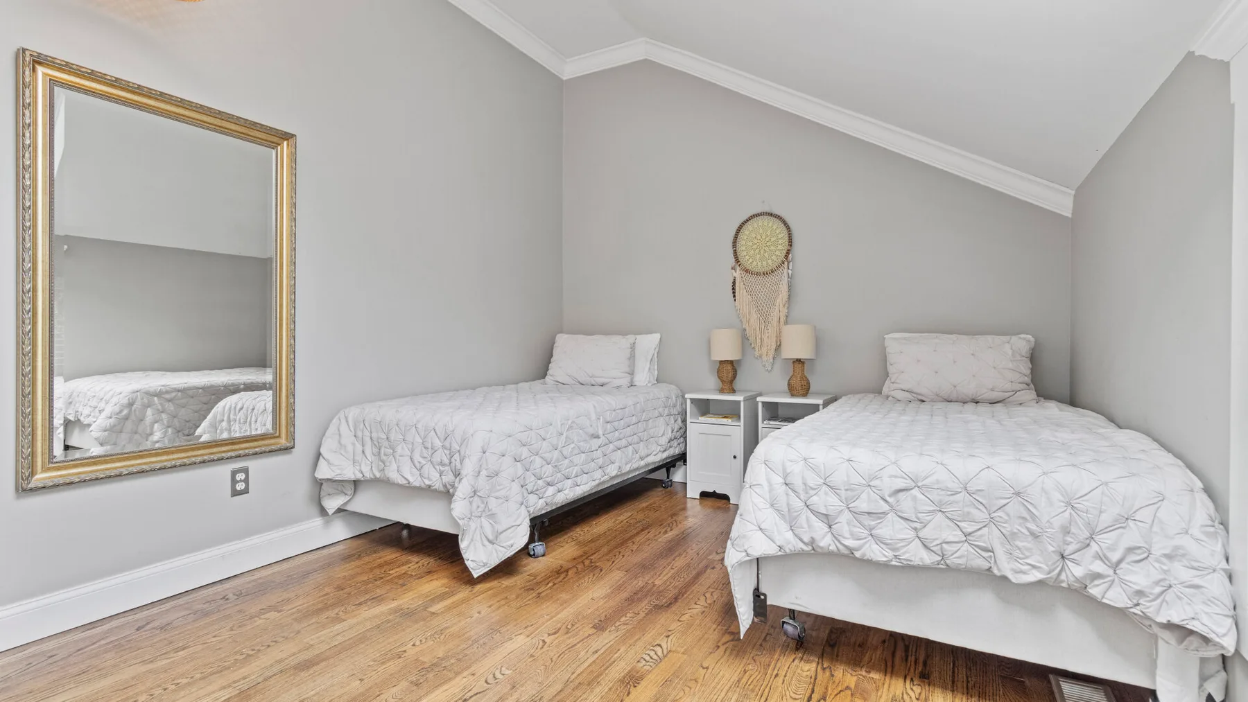 A bedroom with two beds, bedside tables, and a large wall mirror.