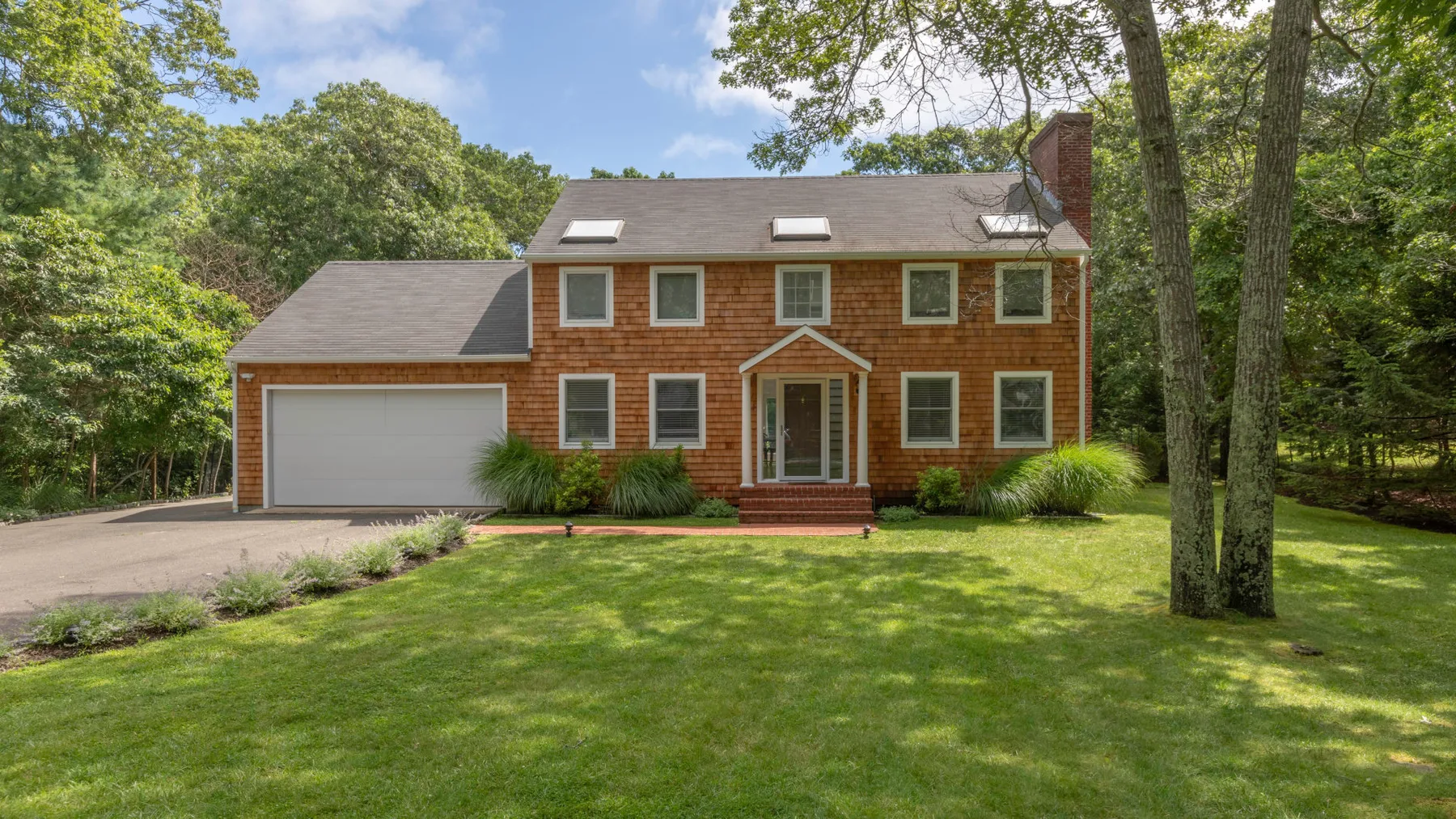 A red-brick house with a garage stands beside a broad green lawn.