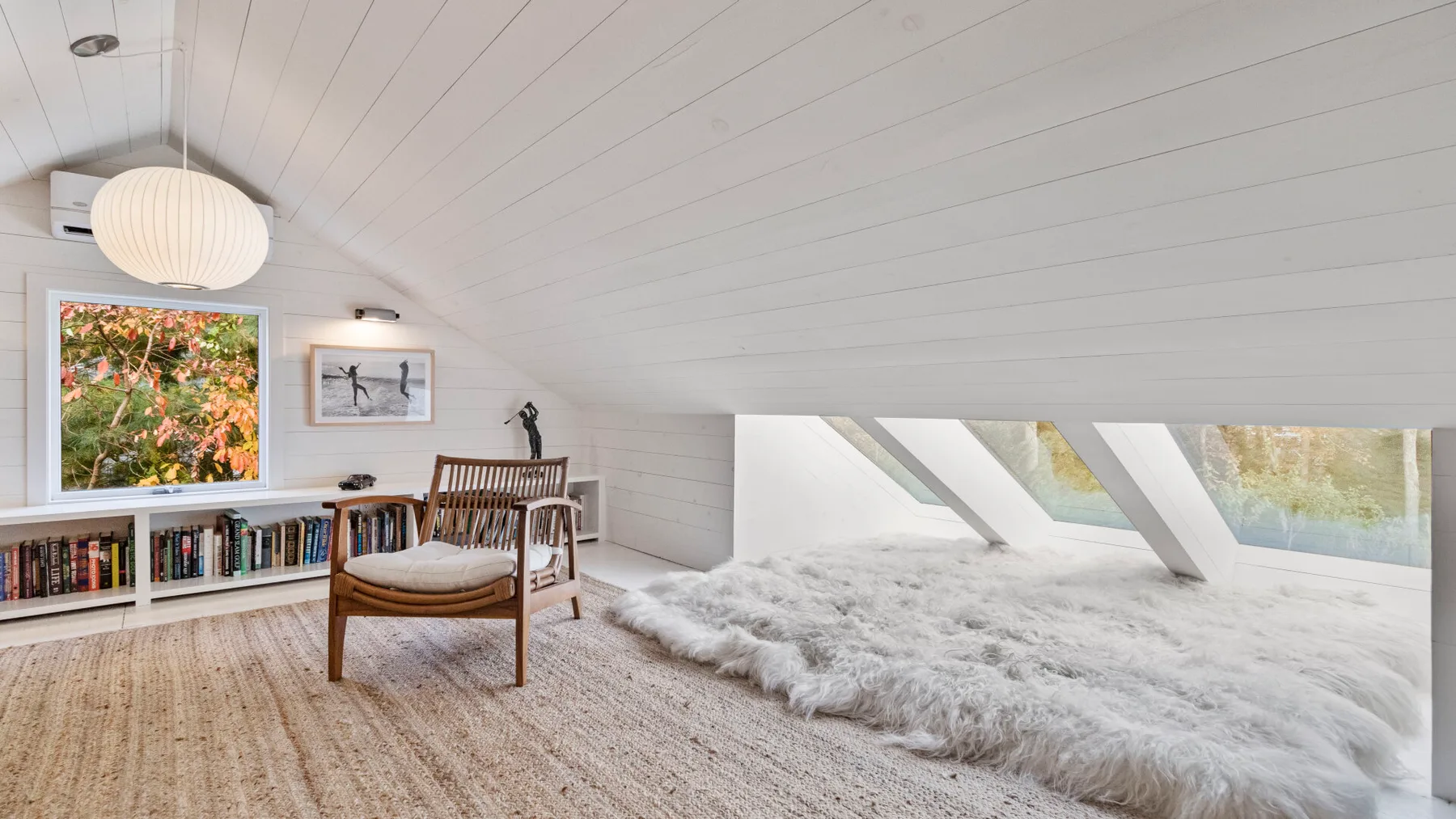 A bright attic reading nook with bookshelves, seating, and a sloped ceiling.