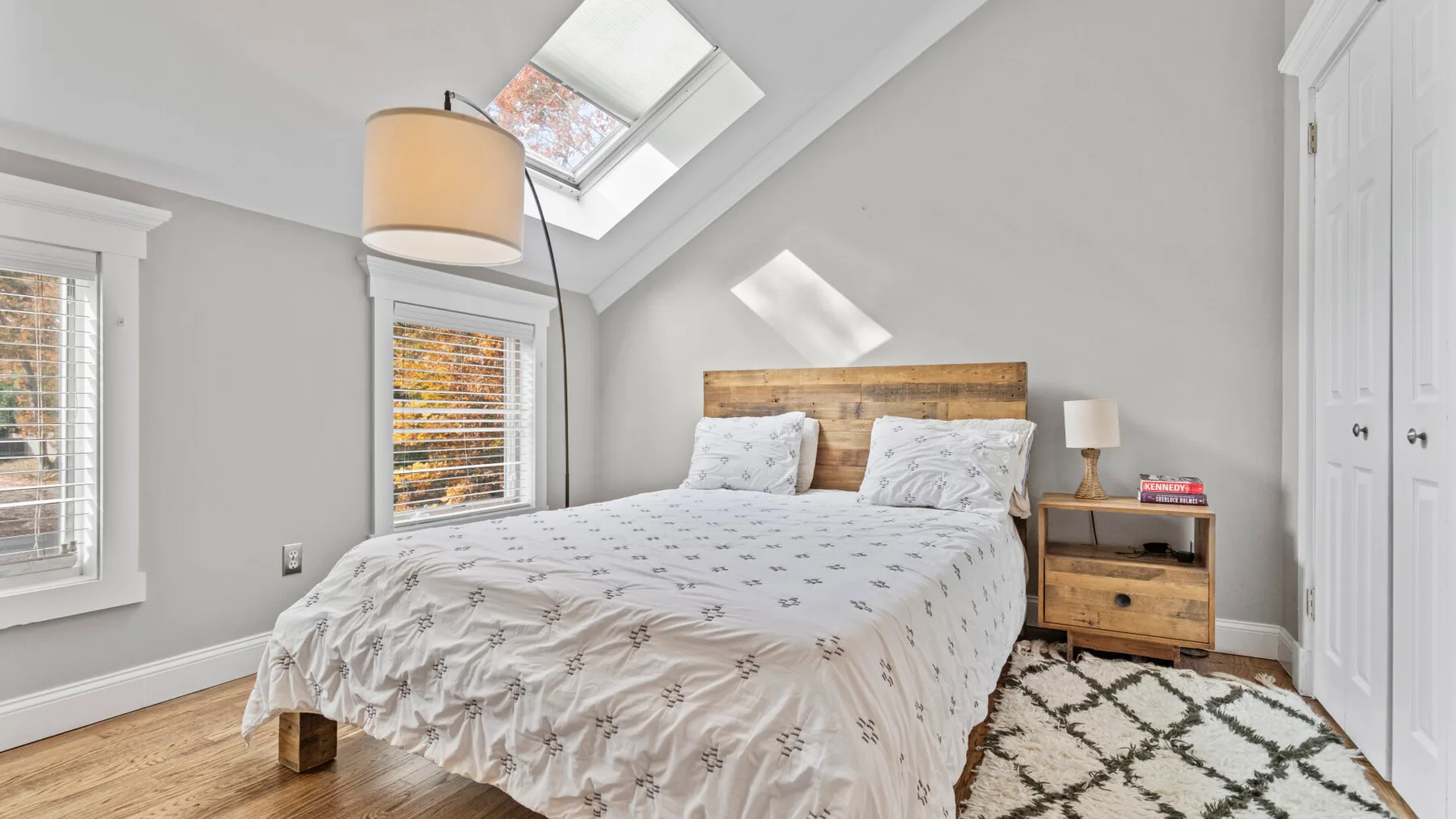 A bright bedroom with a double bed beneath a sloped ceiling and skylight.