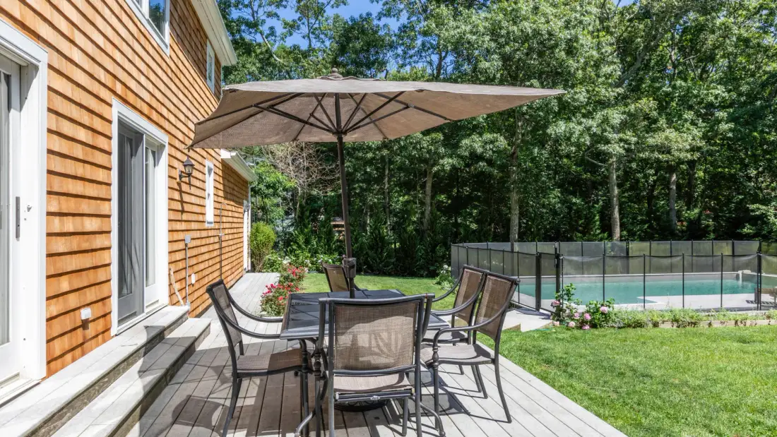 An outdoor dining area with a large umbrella beside a lawn and swimming pool.
