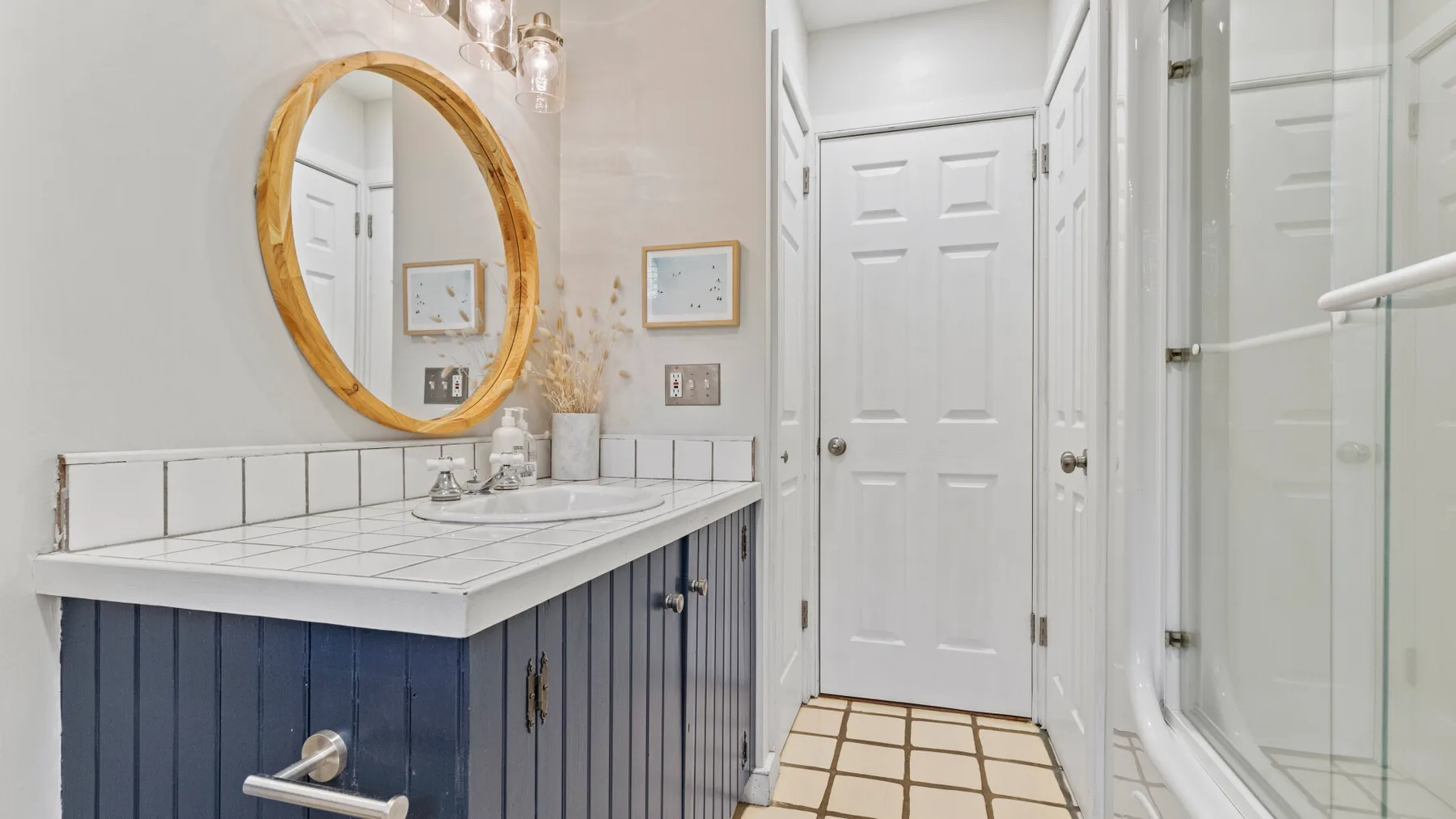A bathroom vanity with a round mirror beside a glass shower.