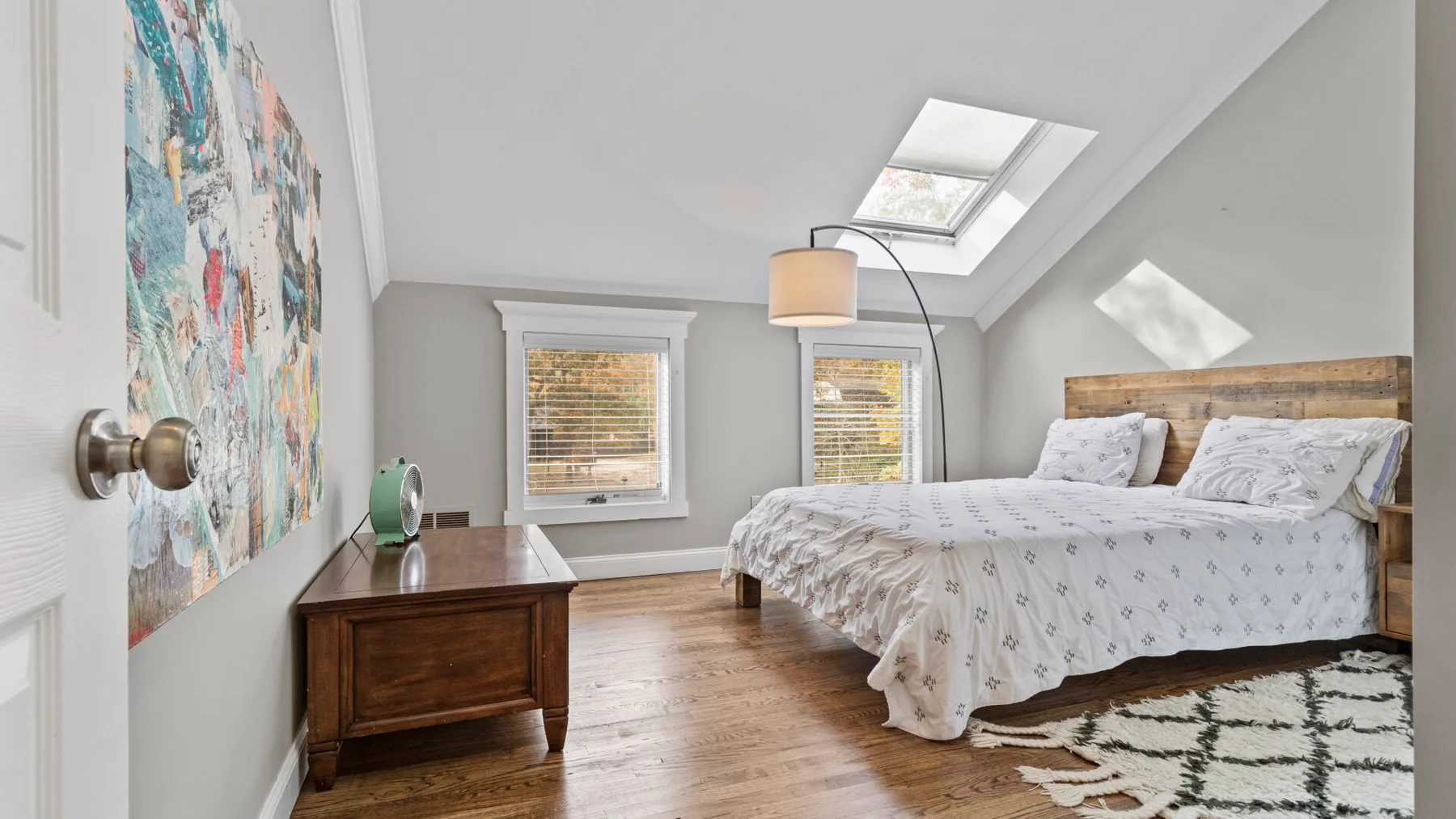 A bright bedroom with a wooden bed beneath a skylight.