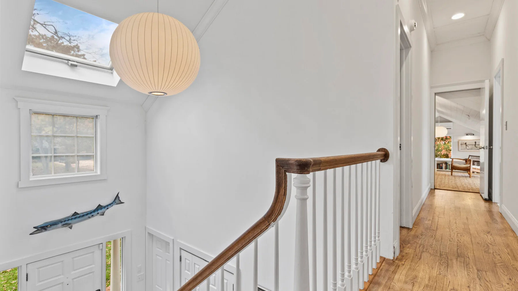 A bright staircase landing with a large hanging light and a hallway beyond.