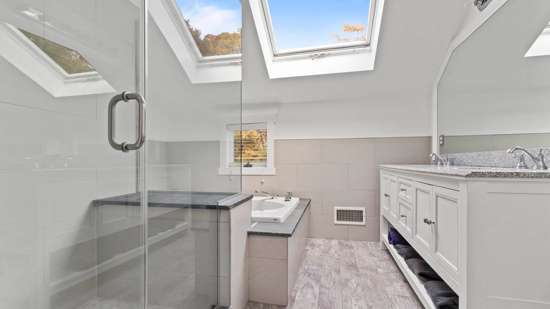 A bright bathroom with a glass shower, vanity, and skylights.