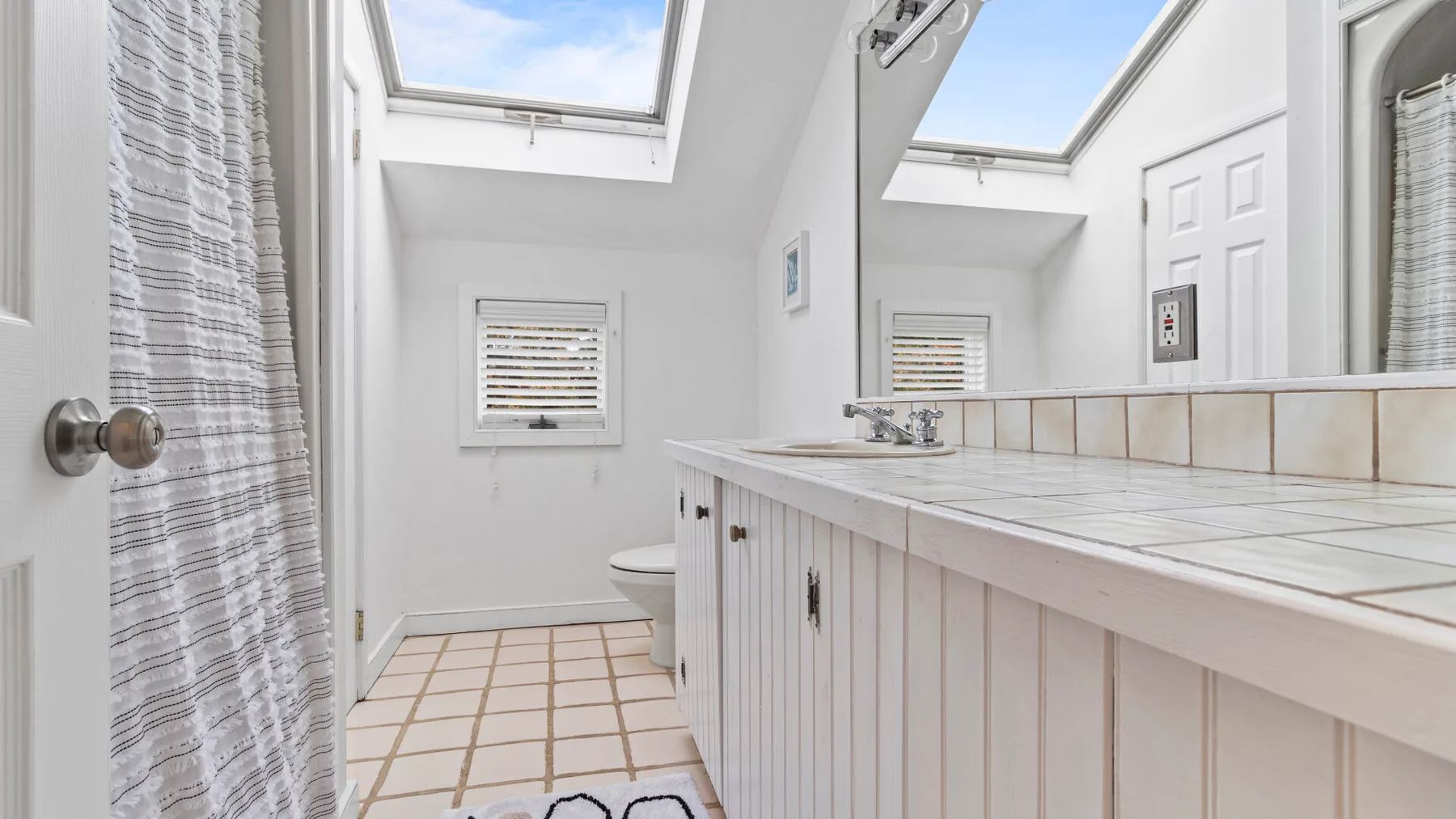 A bright bathroom with a tiled floor, long vanity, and skylights.