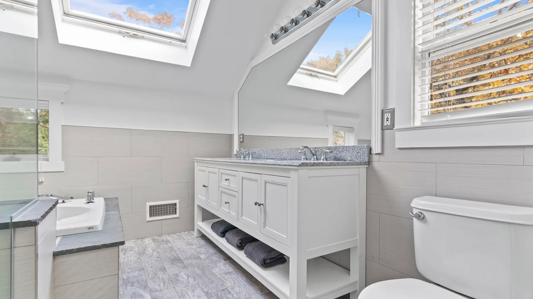 A bright bathroom with a double-sink vanity, bathtub, and skylights.