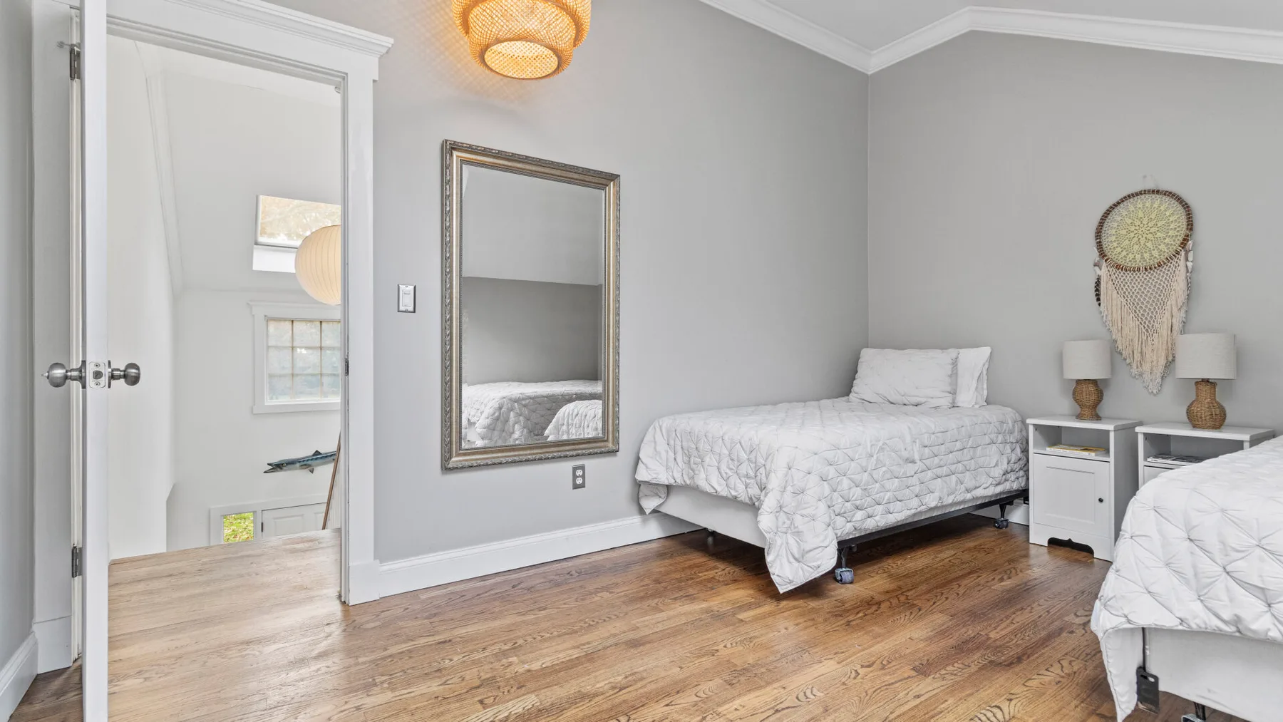 A bedroom with two beds, a mirror, and light wood flooring.