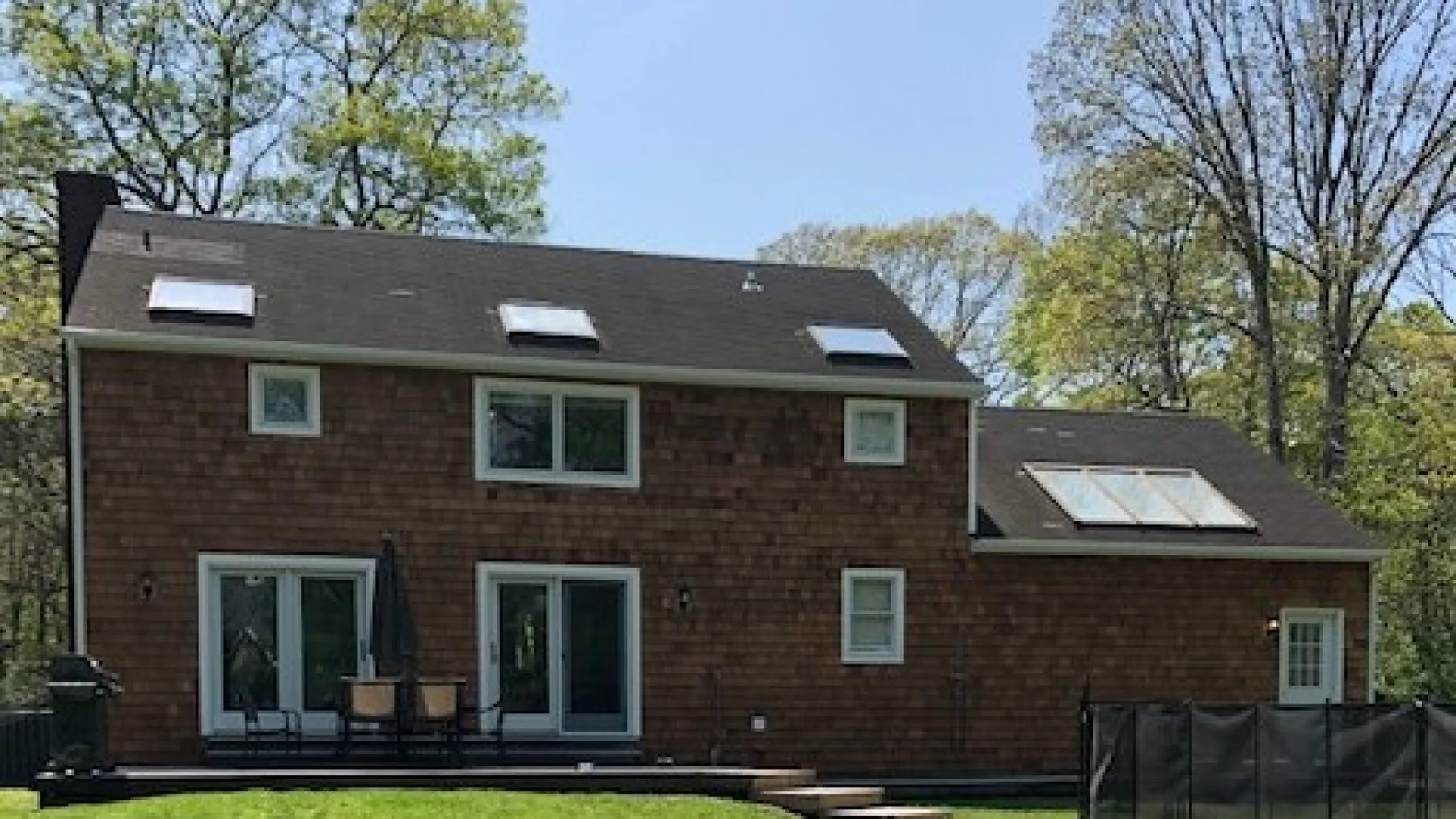 A brick-sided house stands among trees, with a patio and outdoor seating.