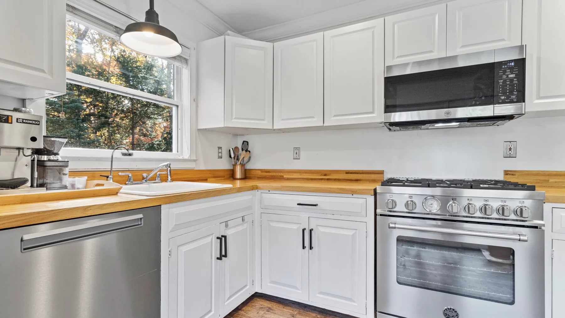 A bright kitchen with white cabinets, wooden countertops, and stainless steel appliances.