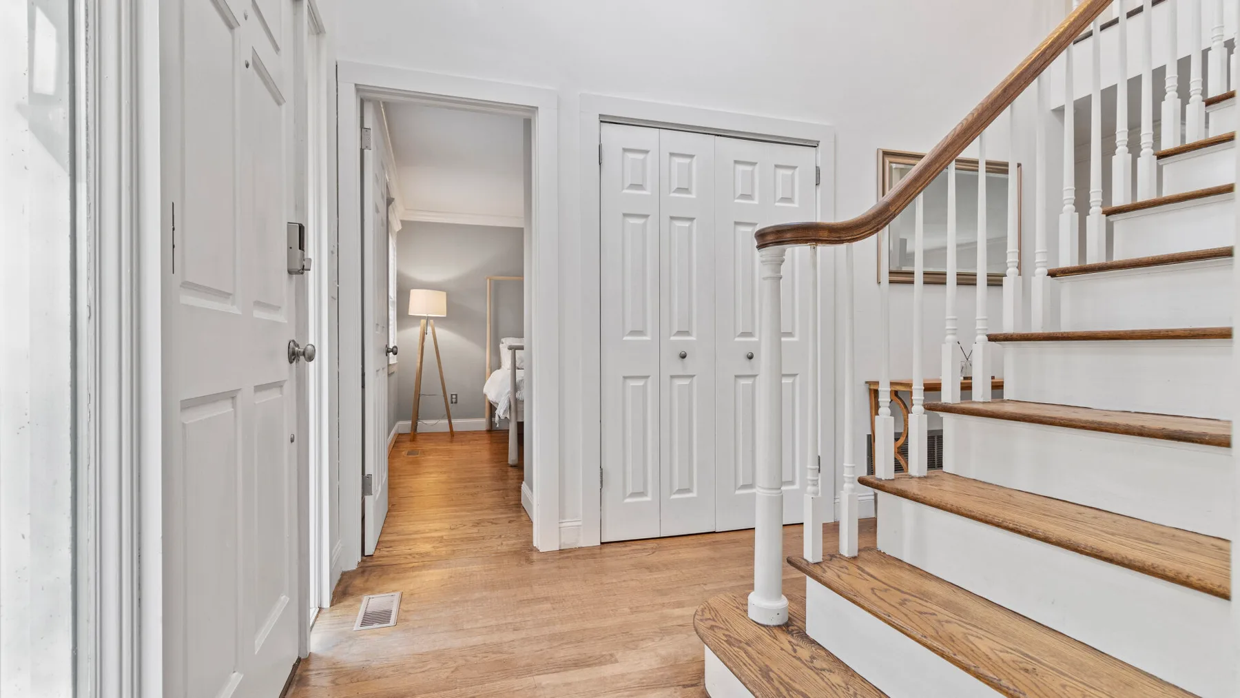 A bright interior hallway with a wooden staircase and several white doors.