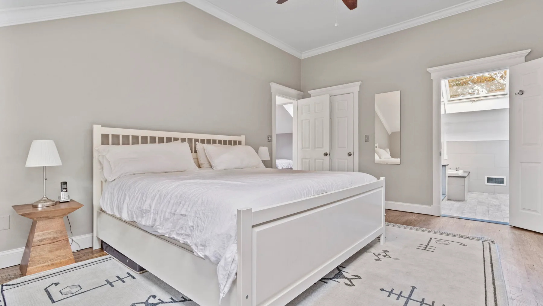 A bedroom with a white bed and a light-colored patterned rug.