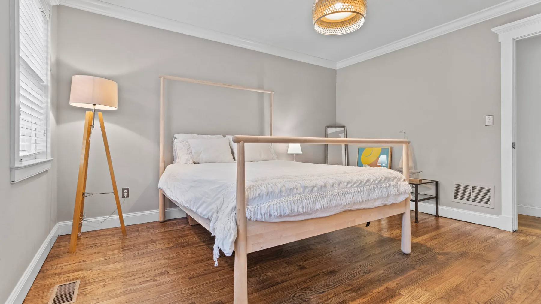 A bedroom with a bed, a floor lamp, and wood flooring.