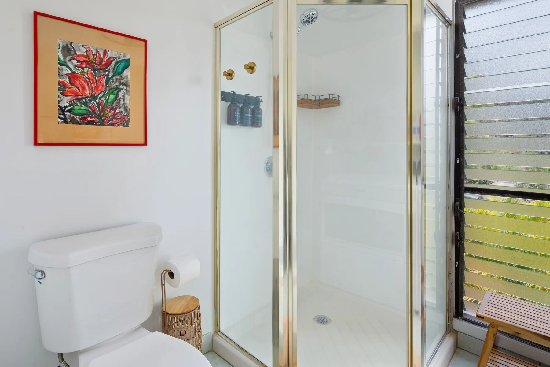 A bathroom with a glass shower, toilet, and framed wall art.